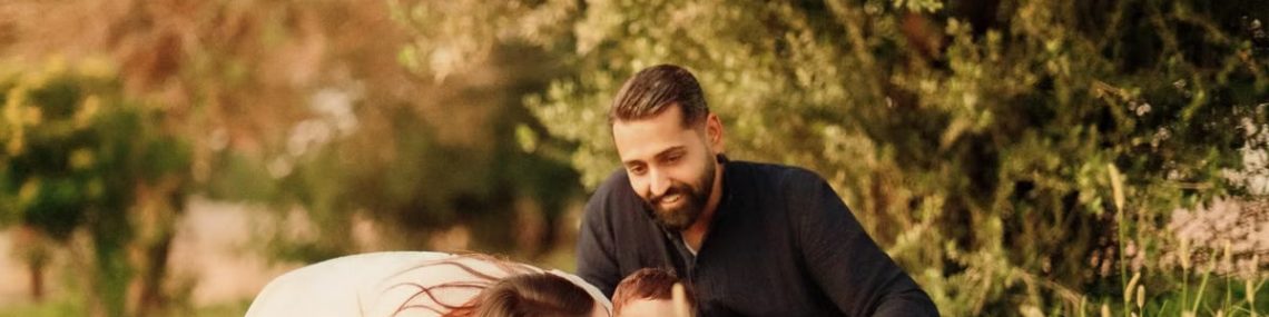 A joyful family with parents and a baby enjoying a sunny day outdoors on a picnic.